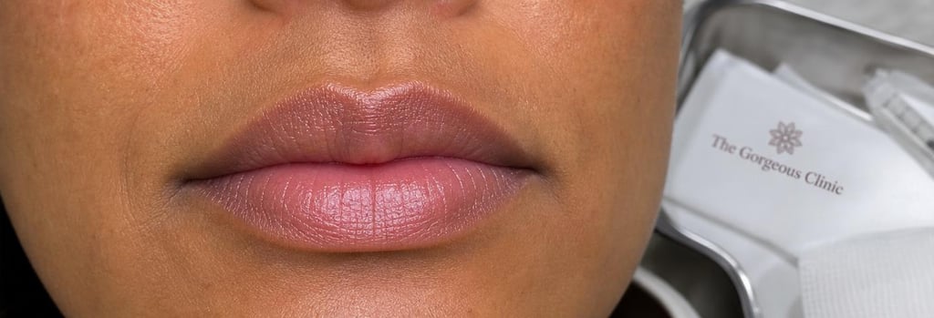 Photorealistic close-up of lips in soft clinical lighting, woman of ethnic origin aged 30s to 50s, natural texture, subtle sheen, shallow depth-of-field, sterile tray or gauze partially visible in background to denote clinical setting.
