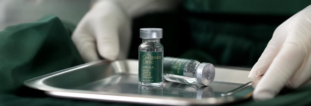 Photorealistic still life of glass vials and gloved hands resting on a sterile tray, shallow depth of field, forest green fabric in soft focus, editorial clinical-luxury feel, single focal point on vials